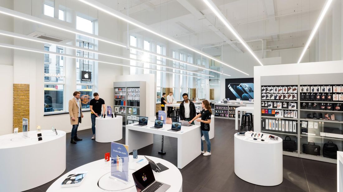 Klanten bekijken en kopen Apple-producten in een Amac-winkel, met zicht op iPads, Macs en accessoires in een modern retailinterieur.